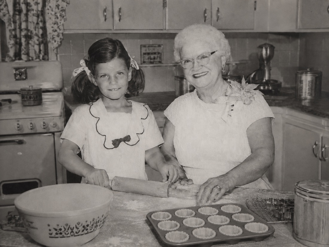 Grandma Allford and a young Amy standing together at a vintage kitchen counter, rolling out dough for tassie shells beside a tin of pressed crusts